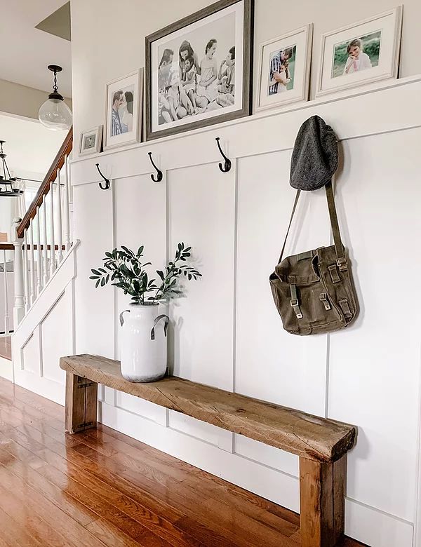 a wooden bench sitting in front of a white wall with pictures on the wall above it