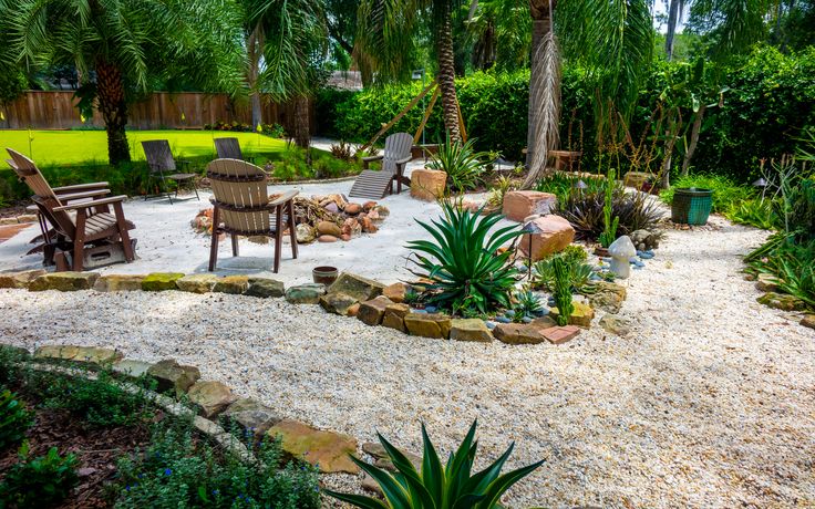 an outdoor patio area with gravel, rocks and plants in the foreground is surrounded by palm trees