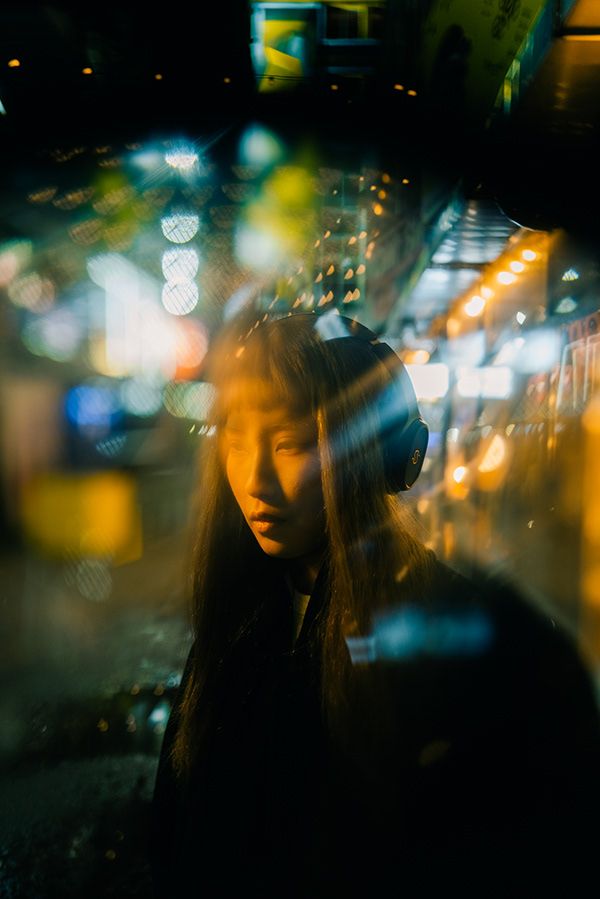 a woman with headphones standing in front of a building at night, looking into the distance