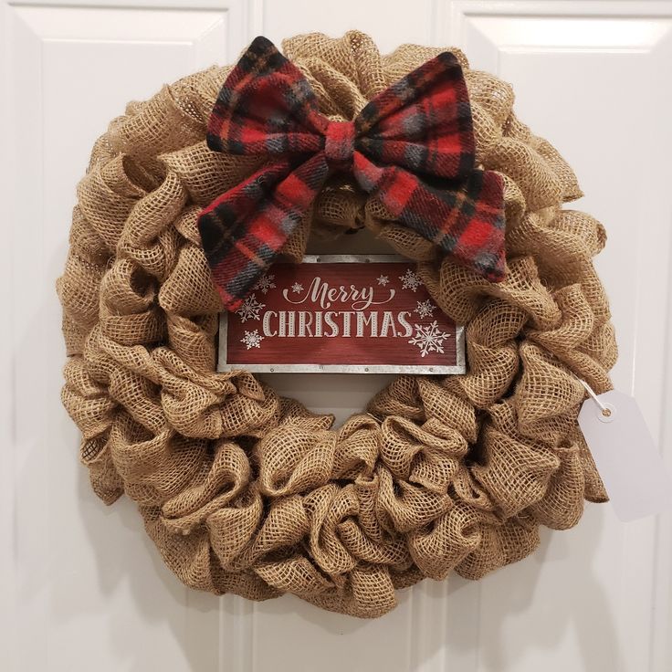 a burlock wreath with a merry christmas sign on it and a bow hanging from the front door