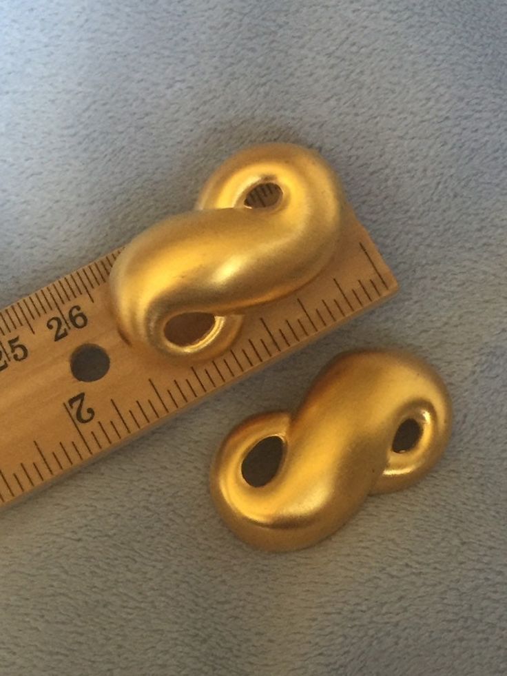 two gold colored buttons sitting next to a measuring tape on top of a blue surface