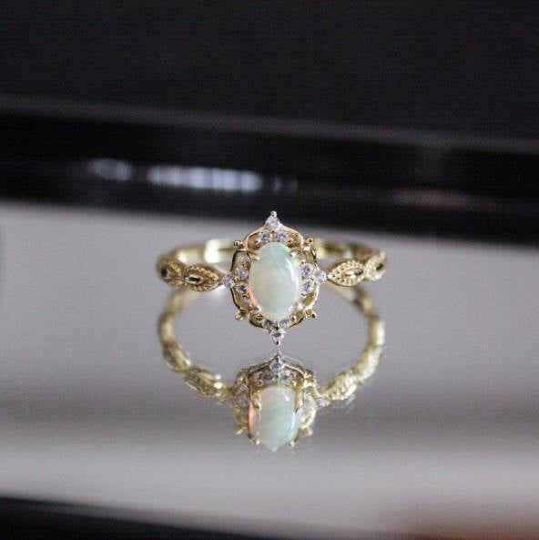 an opal and diamond ring is displayed in front of a mirror