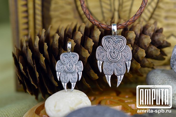 two silver pendants sitting on top of a table next to pine cones and rocks