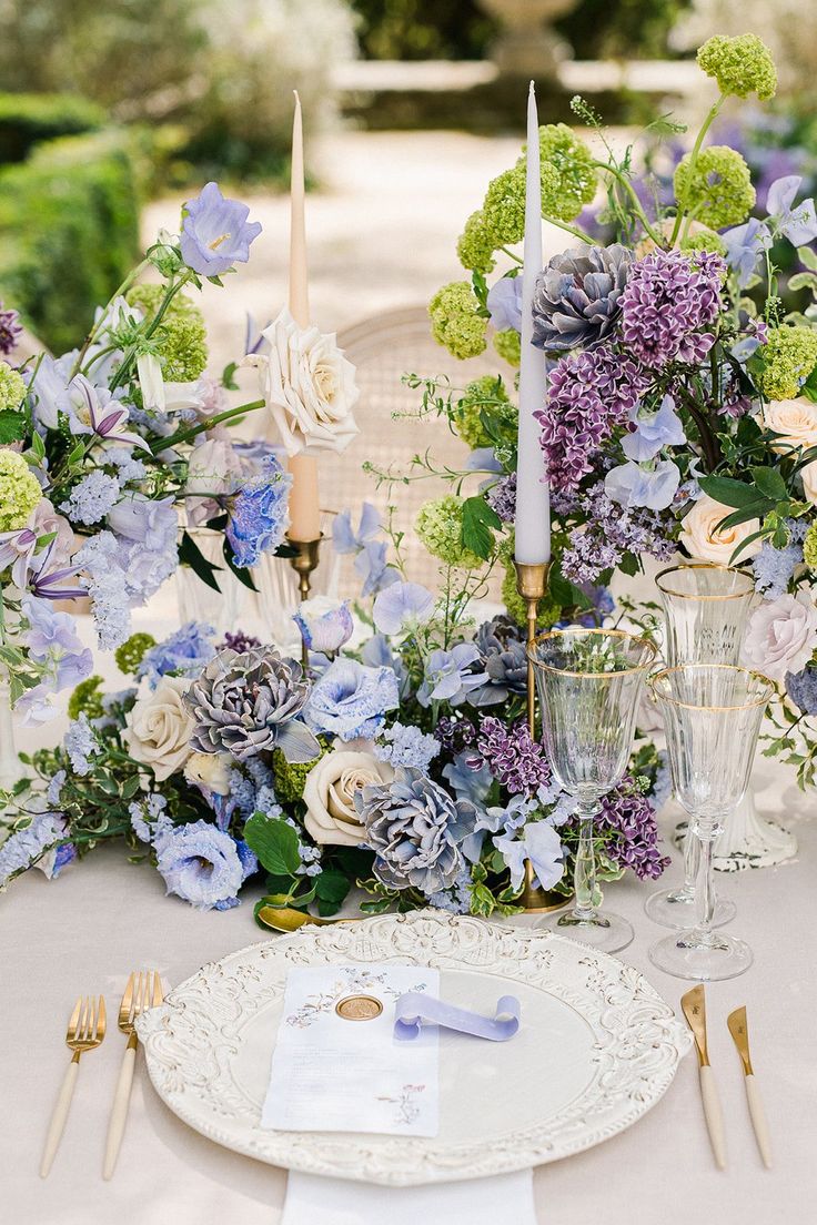 the table is set with blue and white flowers, silverware, and candlesticks