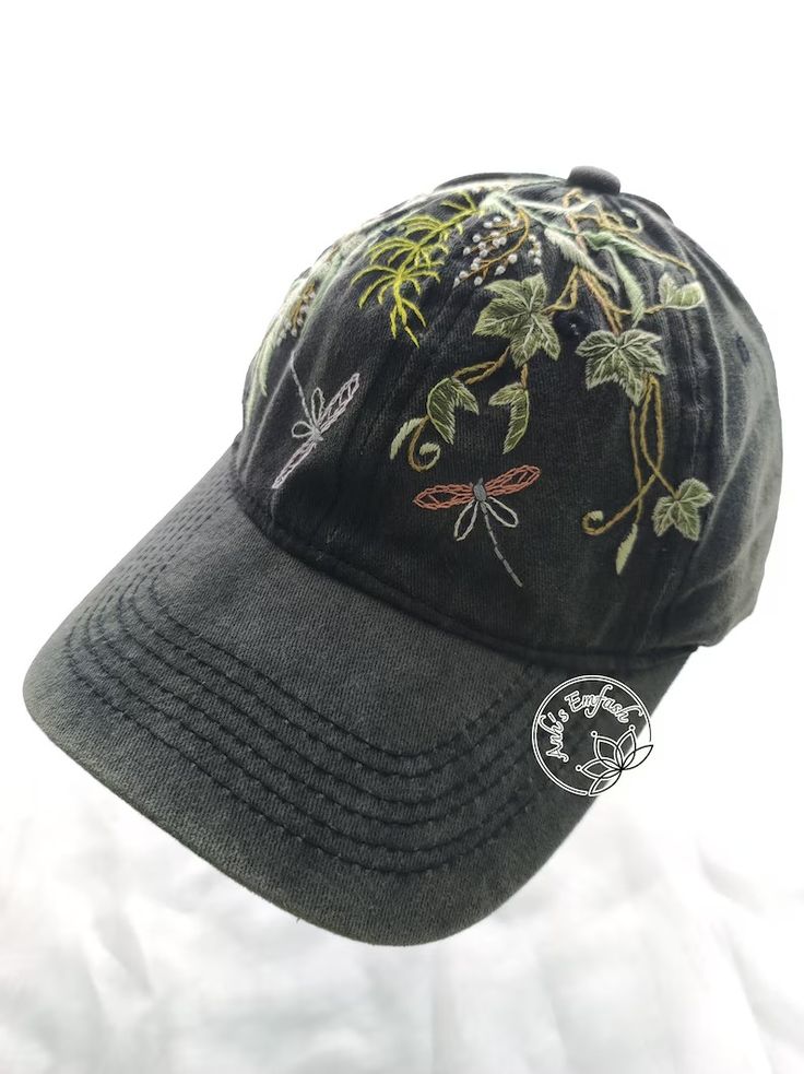 a black baseball cap with dragonflies embroidered on the front and side, sitting on a white sheet