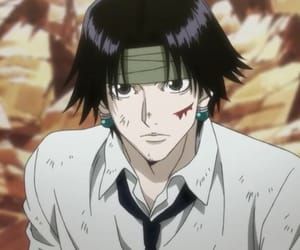 a man with black hair wearing a white shirt and green earrings is staring at the camera