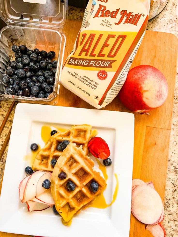 a white plate topped with waffles covered in blueberries and apples next to a carton of milk