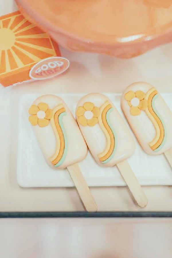 four popsicles sitting on top of a white plate next to an orange bowl and cup