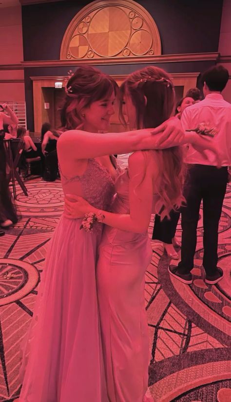 two women hugging each other in front of a room full of people and one is wearing a pink dress