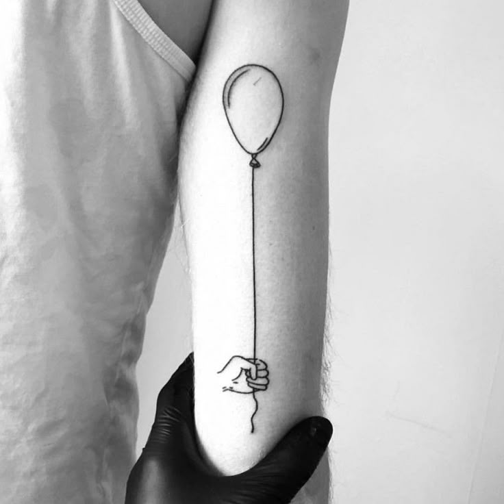 a person with a tattoo on their arm holding a balloon in the shape of a hand