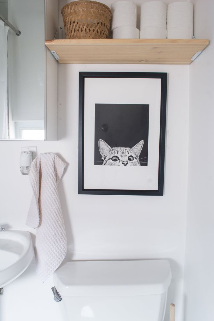 a white toilet sitting next to a bathroom sink under a framed picture on the wall