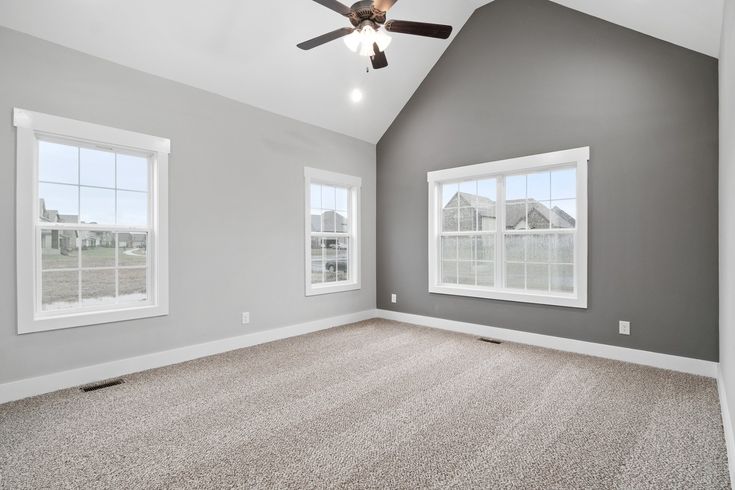 an empty room with two windows and a ceiling fan in the middle of the room