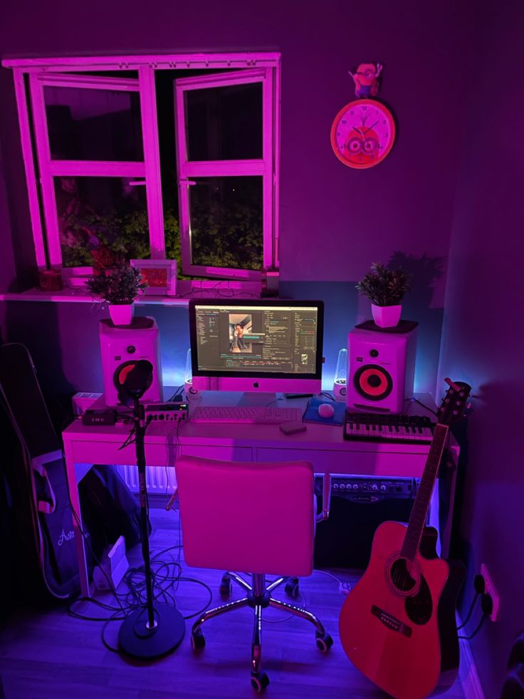 a desk with a guitar, keyboard and monitor in front of a window at night