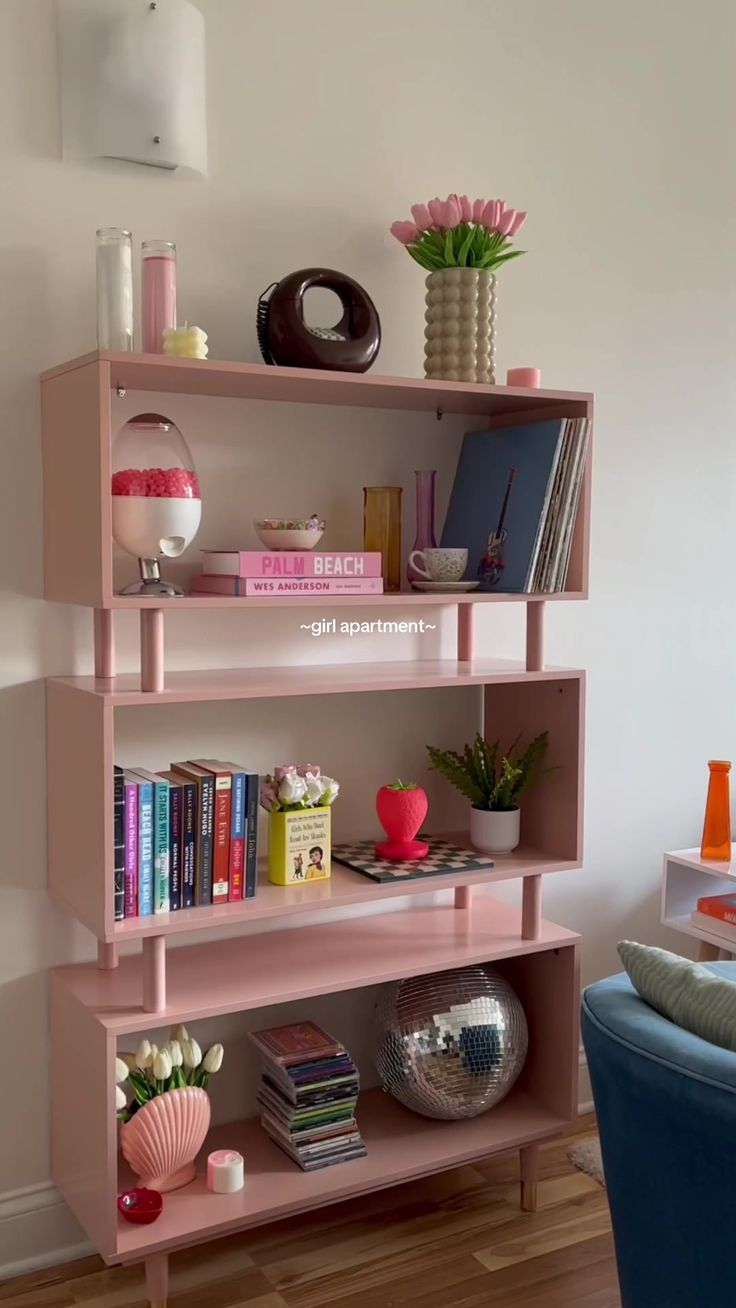 a pink shelf with books and vases on it in a room next to a blue chair