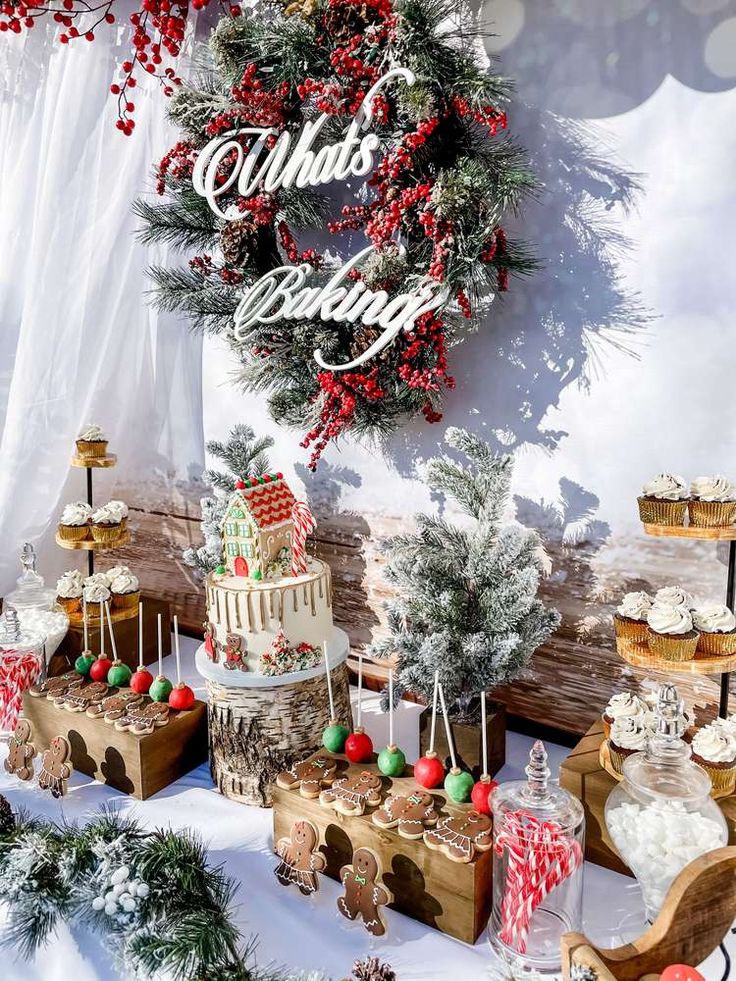 a table topped with lots of cakes and cupcakes next to a christmas wreath