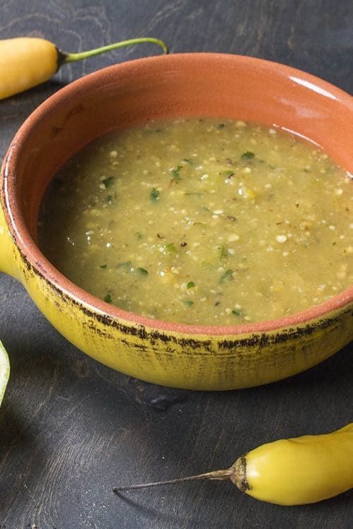 a bowl of soup next to two yellow peppers