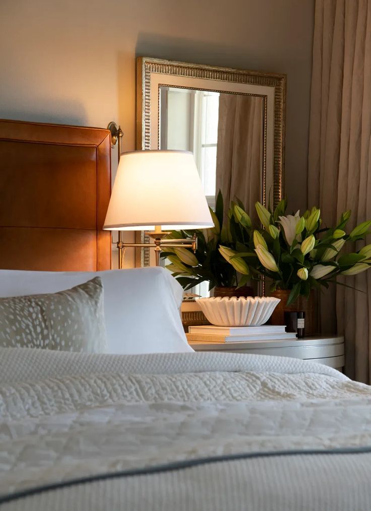 a bed with white sheets and pillows next to a table with a lamp on it