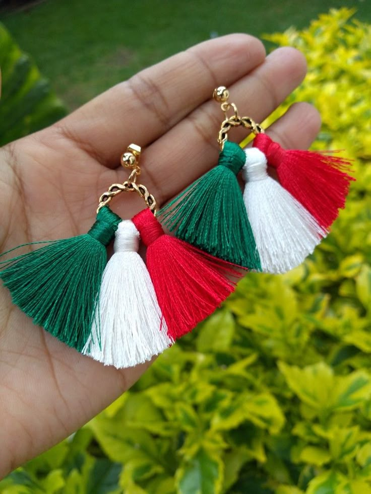 a hand holding two tassels in front of some bushes