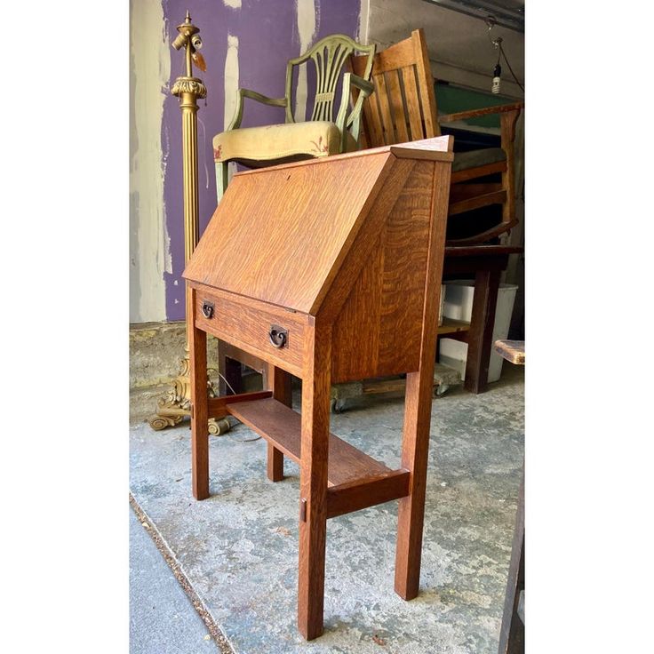 an old wooden desk and chair are sitting on the ground in front of a purple wall