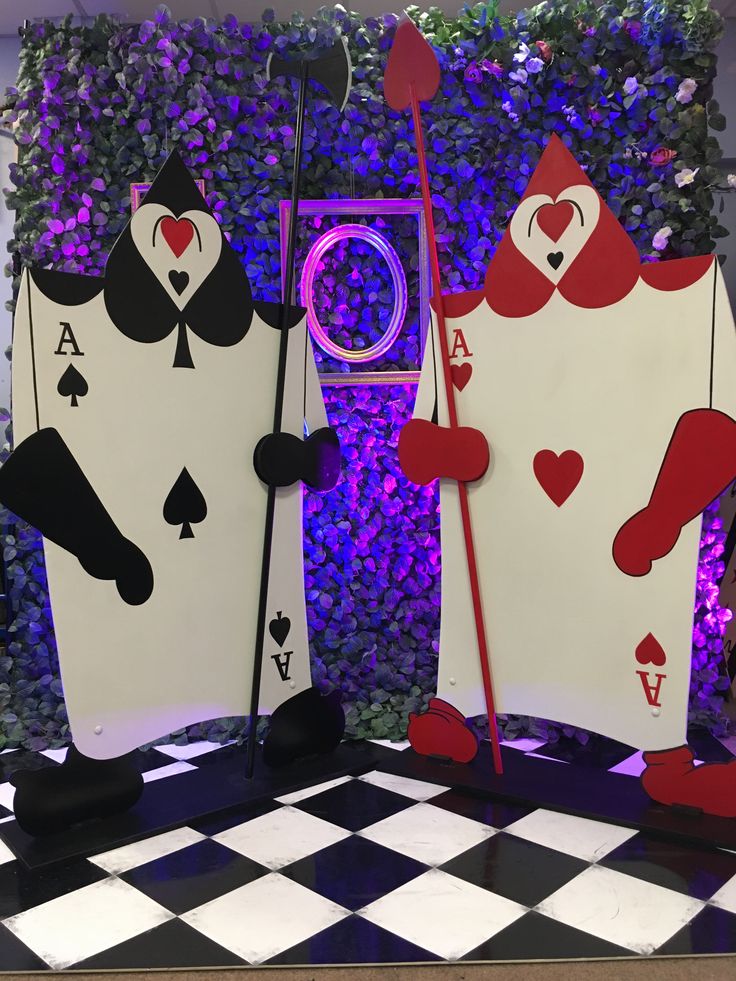 two playing cards are on display in front of a purple wall with plants and flowers