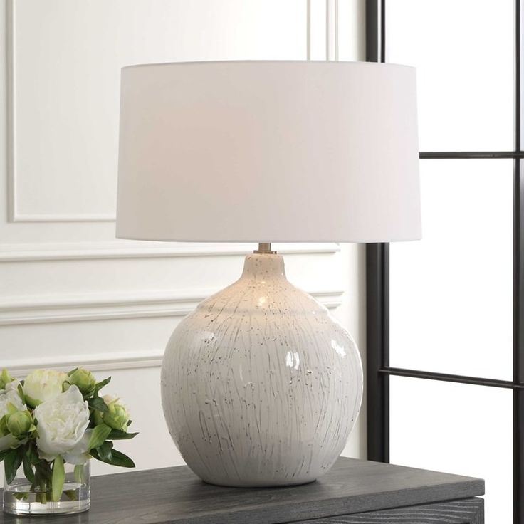 a white lamp sitting on top of a table next to a vase with flowers in it