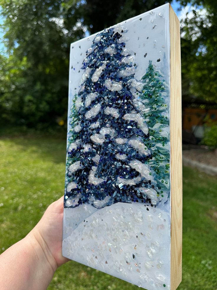 a hand holding up a glass block with a christmas tree on it in the snow