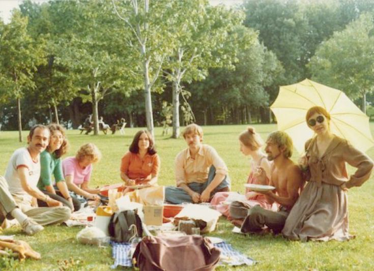 a group of people sitting on top of a lush green field next to each other