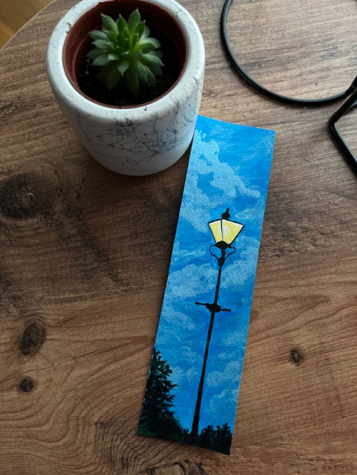 a card with a painting of a street light on it next to a potted plant