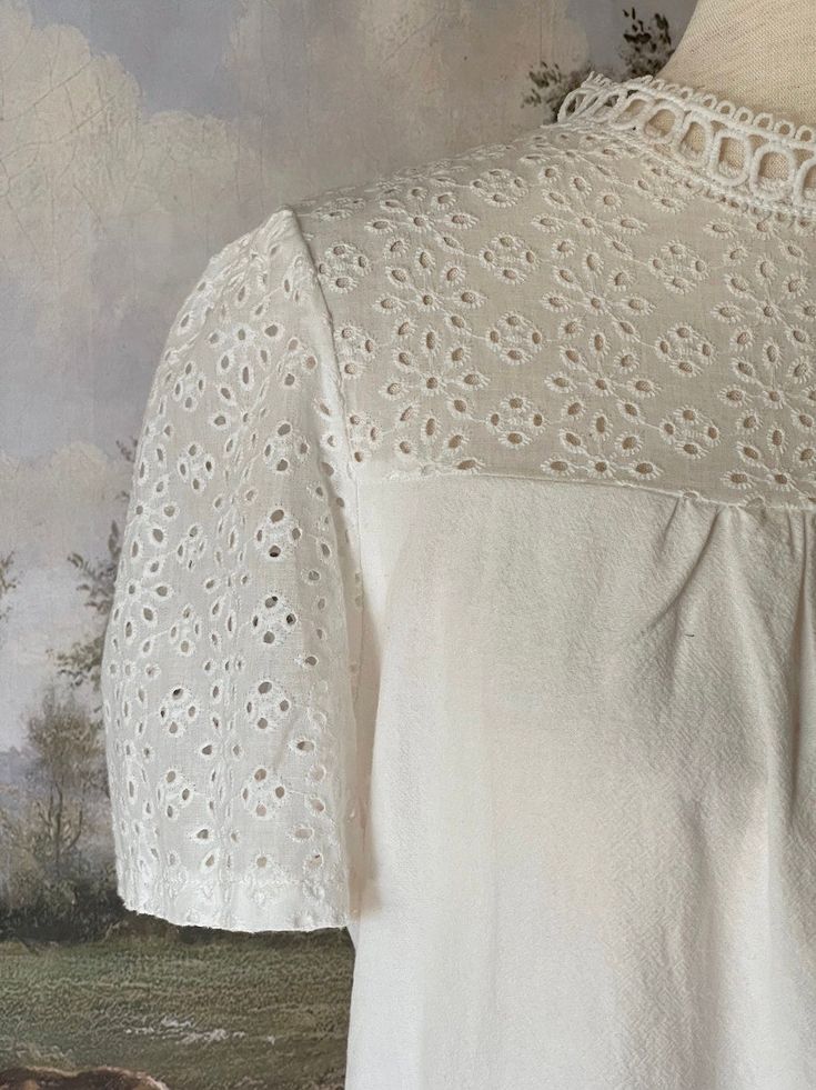 A charming historically inspired blouse that can be used in outfits ranging from the Edwardian era to the 1960's! This piece features a dainty eyelet lace yoke, scalloped lace mock-neck collar, short sleeves, and a gathered bodice. A versatile choice for building your historical wardrobe. This piece is part of our sustainable Secondhand, Vintage, and Upcycled Collection, and thus stock is limited to one! Sizing: Tag size XL, Fits like an XL.Bust up to 44 Inches / 110 CentimetersWaist up to 44 Inches / 110 CentimetersLength - 24.5 / 62 CentimetersSleeve Length - 8 / 22 CentimetersSleeve Width - 8 Inches / 22 Centimeters Condition: B | Some feeling of use, no major flaws. Materials: 100% Polyester synthetic "linen." Short Sleeve Cotton Tops With Scalloped Edges, Cotton Short Sleeve Tops With Scalloped Edges, Cotton Tops With Scalloped Edges And Short Sleeves, Scalloped Edges Tops For Spring Daywear, Scalloped Edges Tops For Spring, Spring Tops With Scalloped Edges For Daywear, Feminine Cotton Lace Patchwork Top, Elegant Fitted Blouse With Scalloped Edges, Elegant Blouse With Scalloped Edges