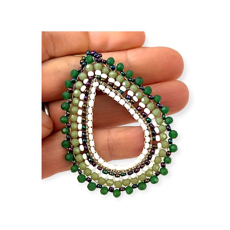 These handmade, green beaded hoop earrings are perfect for anytime. The richly hued shades bring out the color of any outfit. The effect is a concentration of color and interest, sure to turn heads. The earrings come in an array of greens from rich deep forest to light celery complimented by white and iridescent beads for an unusual pattern. The dark green frames the outer side of the tear shaped hoop transitioning to the lighter green, followed by the white with the inner part of the hoop which in turn is framed by the iridescent beads. One of the original artists we discovered created these beautiful statement earrings. He is from a family of talented artists. While we love his talent and the beautiful, creative pieces he makes its - it is his beaming smile and the obvious joy in what he Green Teardrop Hoop Earrings, Green Beaded Teardrop Jewelry, Green Beaded Hoop Earrings For Gift, Green Teardrop Beaded Earrings With Tiny Beads, Green Earrings With Tiny Beads, Green Teardrop Earrings With Tiny Beads, Handmade Green Beaded Hoop Earrings, Green Beaded Dangle Hoop Earrings, Dark Green Beaded Jewelry With Round Beads