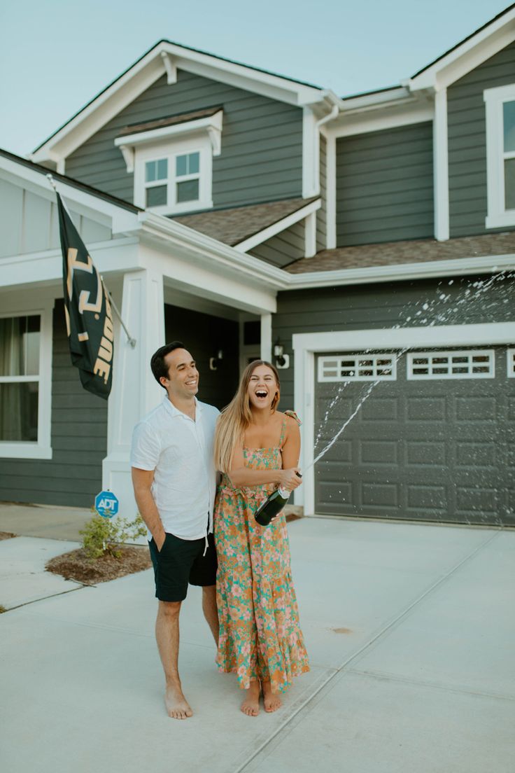 a man and woman standing in front of a house with a sprinkler