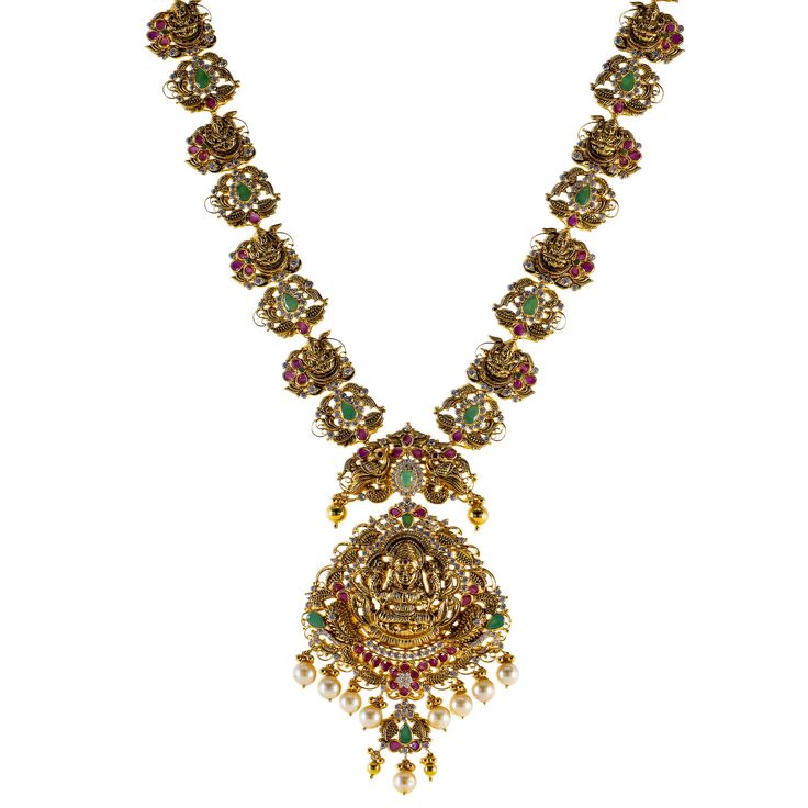 Featuring an elegant blend of ruby, emerald, pearls, and cubic zirconia stones, this 22k antique gold Temple necklace set from Virani Jewelers pays homage to classic Indian temple jewelry. The intricate craftsmanship highlights the stunning gemstones, while the antique 22k gold finish gives the set an heirloom-like quality. This piece of Indian gold jewelry seamlessly blends tradition and sophistication, making it a perfect choice for those who value the artistry of heritage designs in modern jewelry collections.Features• 22k yellow gold• Antique finish• Engraved details• Cubic zirconia• Pearls• Ruby Specifications:• Minimum Width - 2.3 millimeters• Maximum Width - 58.5 millimeters• Length - 30 inches• Weight - 90.9 grams Temple Jewellery Tarinika Jewelry, Gold Necklace Indian Bridal Jewelry Kameswari Jewellers, South Indian Diamond Jewellery Necklaces, South Indian Bridal Jewelry Sets Diamond, Uncut Diamond Necklace Kameswari Jewellers, Antique Gold Jewelry Indian Necklaces Kameswari Jewellers, Antic Gold Jewellery Necklace, Ruby Jewelry Necklaces Kameswari Jewellers, Luxury Ruby Temple Necklace With 17 Jewels