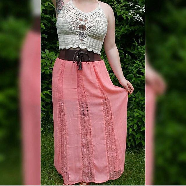 a woman wearing a pink skirt and white tank top standing in front of some bushes