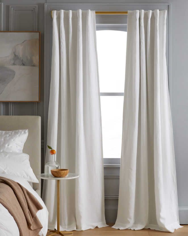 white curtains hanging in front of a window with a painting on the wall behind it