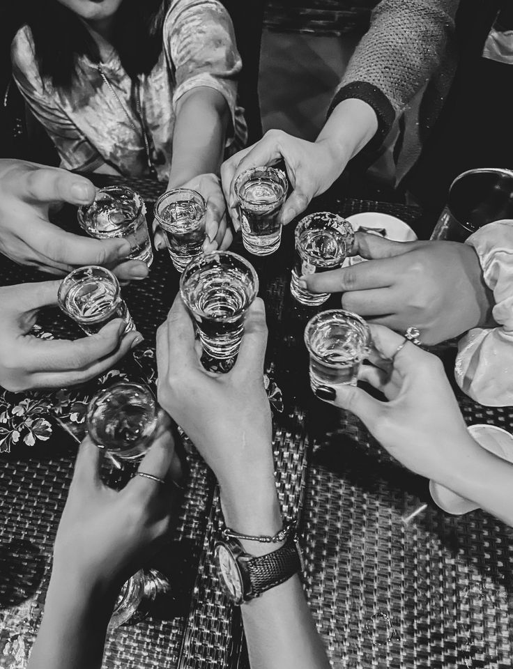 a group of people sitting around each other holding glasses with drinks in them on top of a table