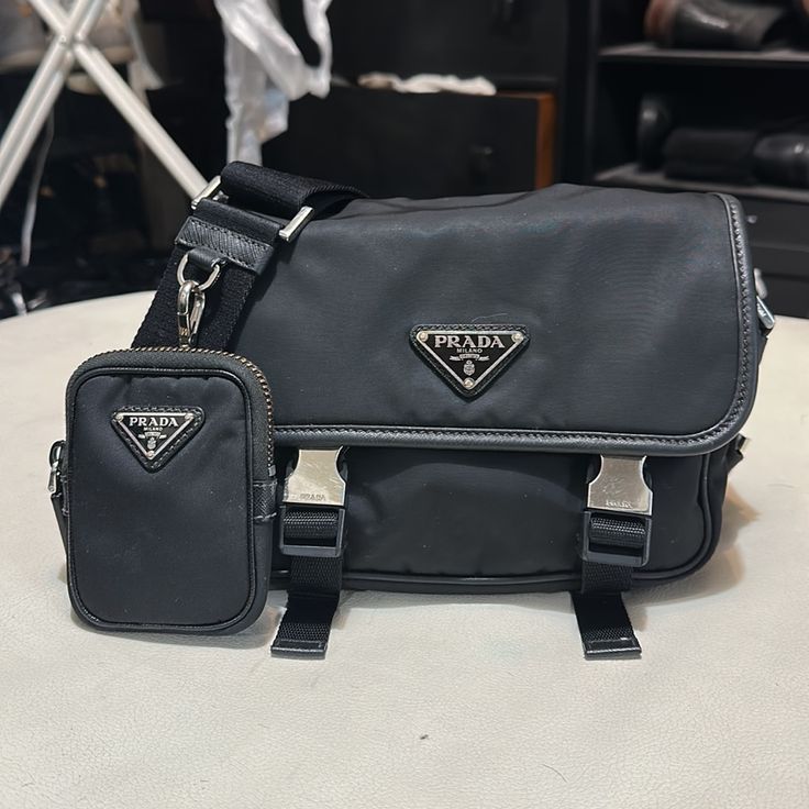 Prada Re-Nylon And Saffiano Leather Shoulder Bag Unisex Also Posted Hat Separately M Nice Conversation/ Status Piece Great Bag, Preserved Very Well Reduced Price Due To Minor Flaws Comes With Box Taking Offers - Small Pouch Zipper Fading( No One Pays It Any Attention)As Shown In Pic. I Had Small Pouch Hook Strap Reinforced To Keep From Tearing Away From The Leather( Also Unnoticed)As Shown In Pic Waiting For A New Home Luxury Black Shoulder Bag With Silver-tone Logo, Designer Black Shoulder Bag With Silver-tone Logo, Designer Black Bag With Silver-tone Logo Plaque, Designer Black Bag With Silver-tone Logo, Small Pouch, Small Pouches, Zipper Pouch, Leather Shoulder Bag, New Home