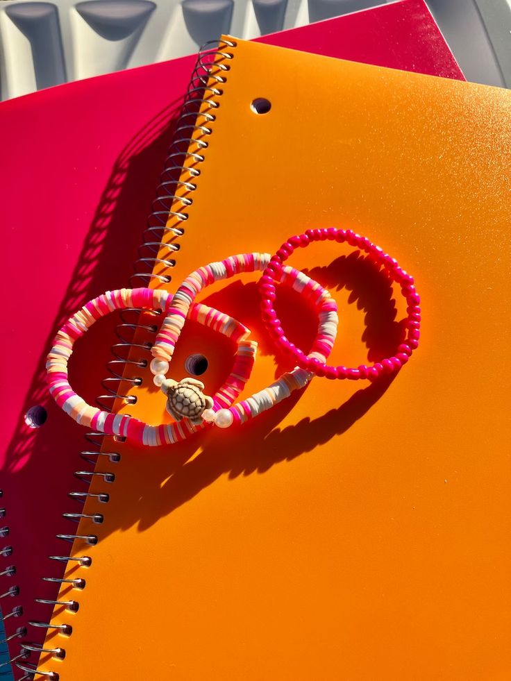 two spiral - bound notebooks with pink and white beads on them sitting next to each other