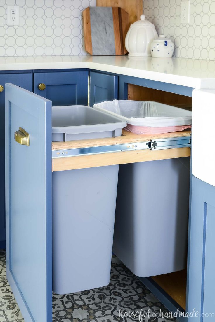 a kitchen with blue cabinets and two trash cans in the cabinet door, next to a white counter top