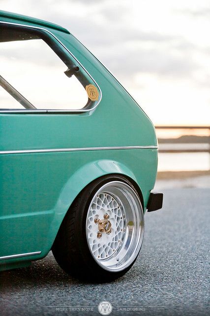 the front end of a green car with chrome rims and spokes on it