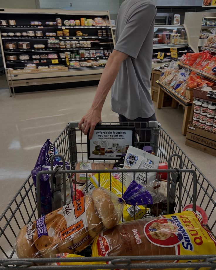 a man pushing a shopping cart full of food in a grocery store with other items