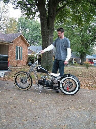 a man standing next to a parked motorcycle in front of a house with a truck behind him