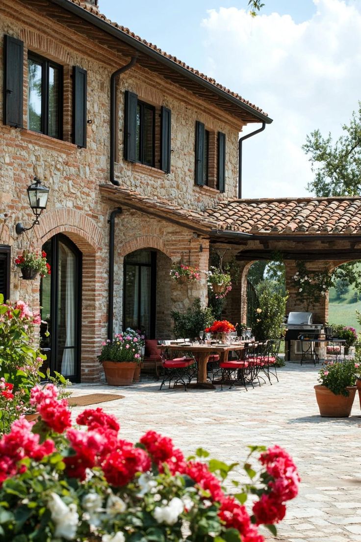 an outdoor patio with potted plants and flowers in the foreground, next to a large brick building