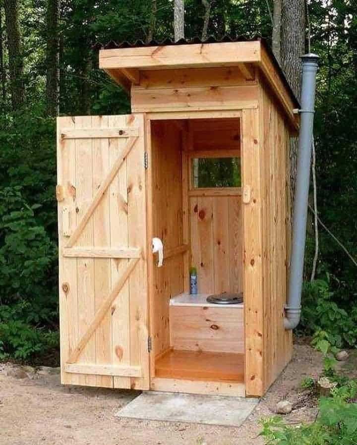 a wooden outhouse in the woods with its door open and water coming from it