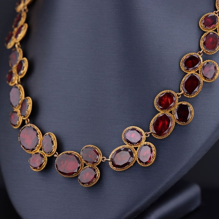 Experience the timeless elegance of this remarkable antique necklace dating back to the late Georgian era (circa 1820). Crafted with meticulous artistry, this exquisite piece showcases 54 oval flat-cut, foil backed garnets, set in 14k bloomed gold with closed backs, preserving their radiance for centuries. Measuring 16 inches in length, this antique necklace exudes a captivating charm and is in overall good condition. While there is one visible surface-reaching inclusion, it adds to the characte Opulent Formal Necklaces With 17 Jewels, Opulent Round Necklaces For Formal Occasions, Luxury Oval Jewelry For Opera, Antique Gold Jewelry For Opera, Luxury Oval Jeweled Necklaces, Luxury Jeweled Oval Necklaces, Formal Oval Necklace With 17 Jewels, Victorian Oval Jewelry For Opera, Formal Oval Necklaces With 17 Jewels