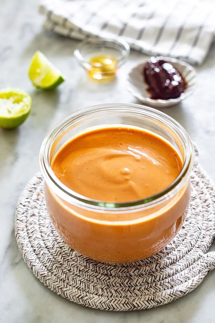 a glass jar filled with sauce sitting on top of a table next to sliced limes