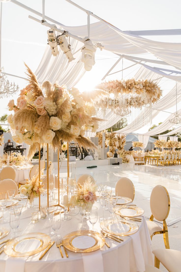 a table set up for an event with white linens and gold place settings on the tables