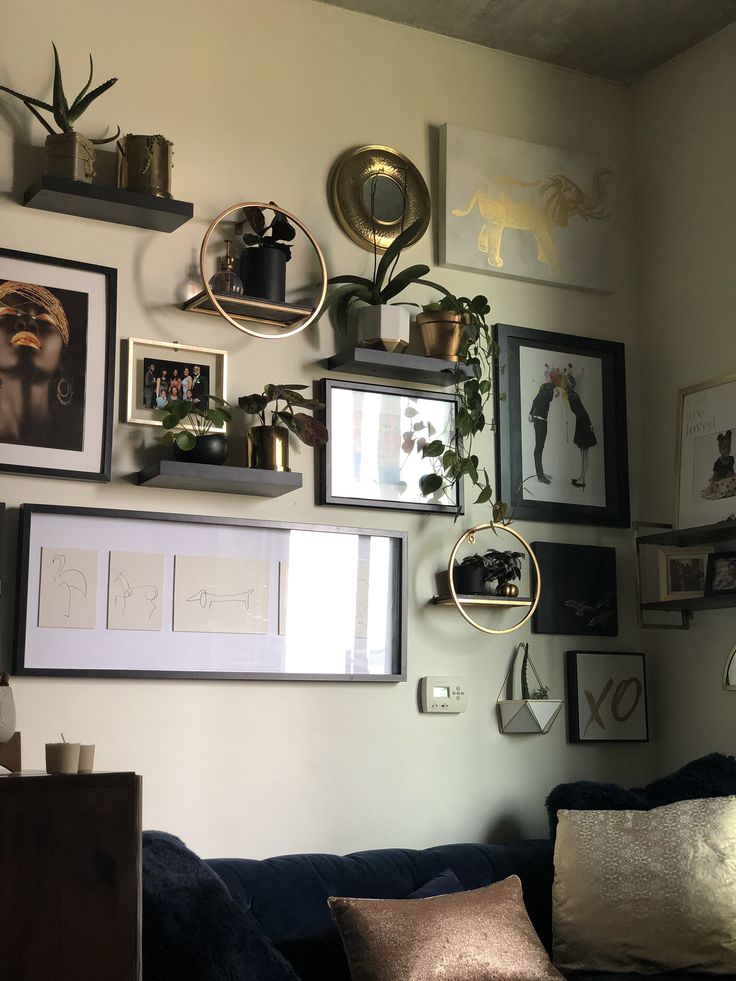 a living room filled with lots of framed pictures and plants on the wall next to a couch