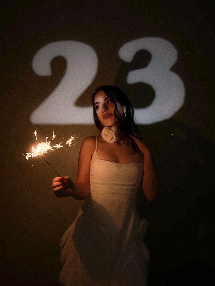 a woman holding a sparkler in front of her face and numbers projected on the wall behind her