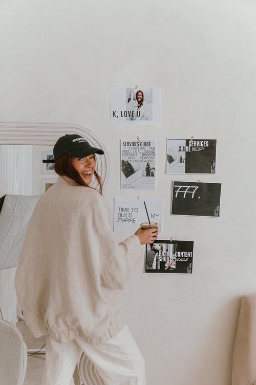 a woman standing in front of a wall with pictures on it and holding a sticker