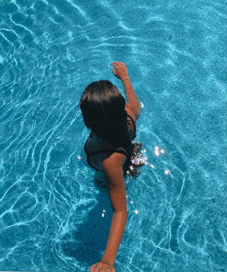 a woman in a black bathing suit standing in a pool with her hand up to the water